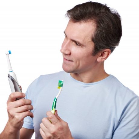 man holding electric and manual toothbrush